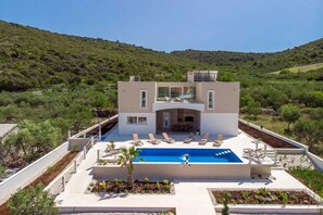 Eine moderne Villa mit Swimmingpool, Liegestühlen und Blick auf die umliegenden Hügel.