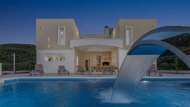 Una casa moderna de dos pisos con piscina, cascada y mobiliario de exterior.