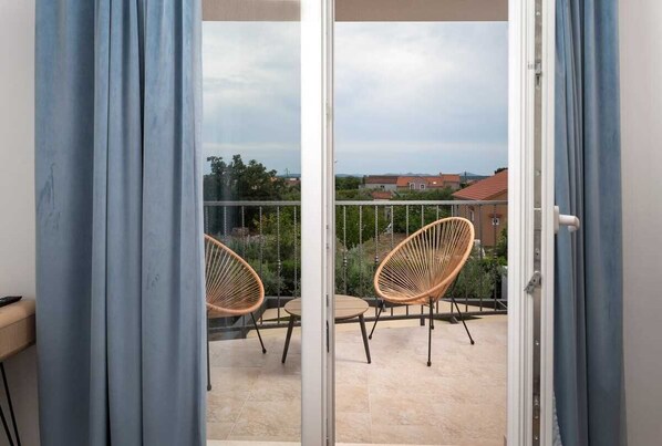 A balcony with two wicker chairs and a table, overlooking a residential area with houses and trees. - Villa Oliva | Adriatic Luxury Villas (Murvica)