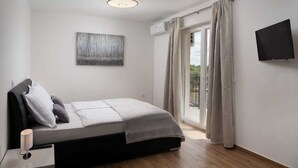 Un dormitorio moderno con cama, televisor de pantalla plana, luz de techo y vistas a través de un ventanal.