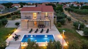 Una casa de dos pisos con piscina, mobiliario exterior y un balcón.
