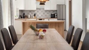 Una cocina moderna con armarios blancos, un refrigerador de acero inoxidable y una mesa de comedor de madera con sillas.