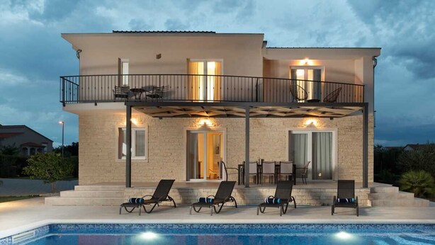 Una casa de dos pisos con piscina, mobiliario exterior y un balcón.