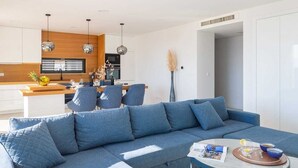 Un salón moderno con un sofá azul, una mesa de centro y una cocina al fondo.