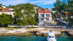 A coastal property with a boat docked in clear water, surrounded by trees and buildings.