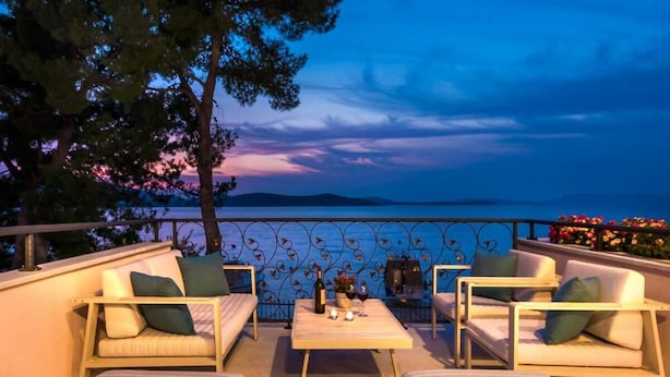 A terrace with outdoor seating, a table, and a view of the sea at dusk.