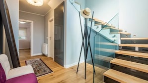 A modern interior with a staircase, a hat on a stand, and a sofa.