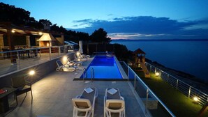 A pool area with lounge chairs and a view of the sea at dusk.