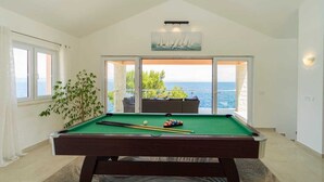 A pool table in a room with a view of the sea through large windows.