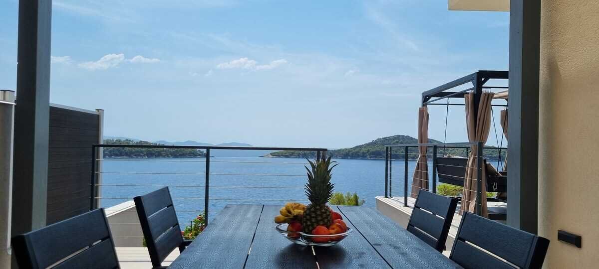 A table with a fruit bowl, chairs, and a view of a lake.
