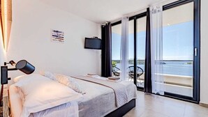 A bedroom with a bed, a TV, a balcony with a view of the sea, and a painting on the wall. - Villa Evia | Adriatic Luxury Villas (Blato)