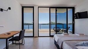 A bedroom with a bed, a desk, and a chair, with a view of the sea through large sliding doors. - Villa Evia | Adriatic Luxury Villas (Blato)