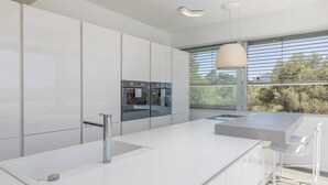 A modern kitchen with white cabinetry, a stainless steel sink, and a large window providing a view of the outdoors.