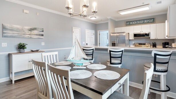 Una cocina moderna con armarios blancos, una isla central con una maqueta de velero y un letrero que dice 'EAT.BEACH.SLEEP.REPEAT'.