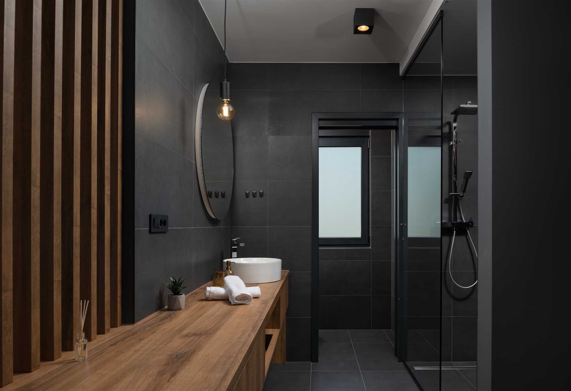 A modern bathroom with a wooden vanity, a white sink, and a glass shower enclosure.