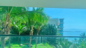 Un balcón con vistas despejadas al agua, palmeras y un edificio moderno al fondo.