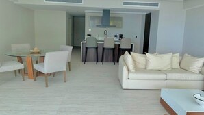 Una sala moderna con una mesa de comedor de cristal, un sofá y una cocina al fondo.