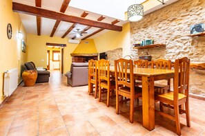Un espace repas avec une table et des chaises en bois, un mur en pierre et un ventilateur de plafond.