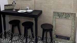 A dining area with a black table, four stools, a chandelier, framed pictures on the wall, and a sign with a wizard-themed message. - Espectacular Apartaestudio Harry Potter (Santa Rosa de Cabal)