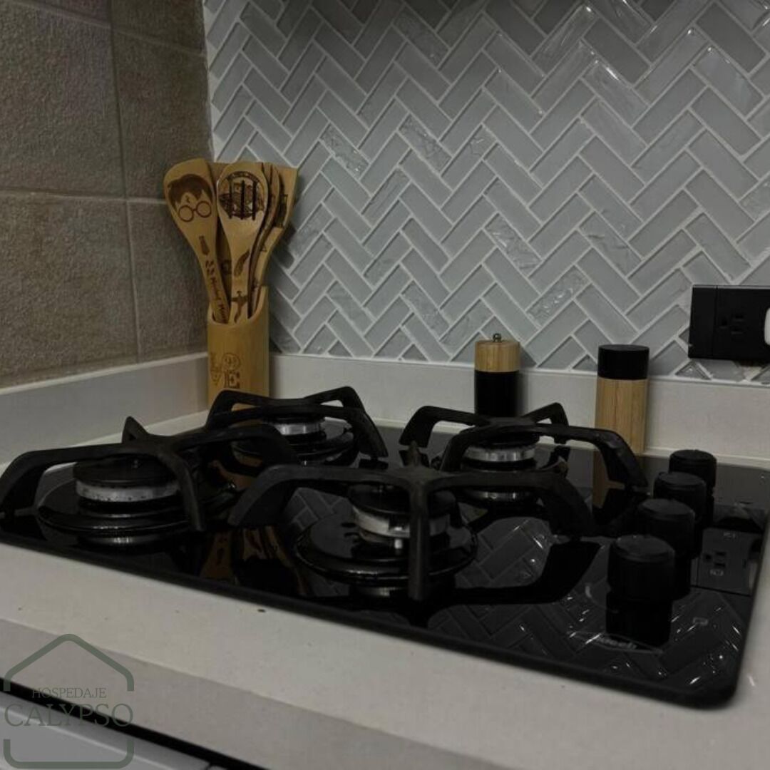 A kitchen with a gas stove, wooden utensils, and a herringbone-patterned backsplash.