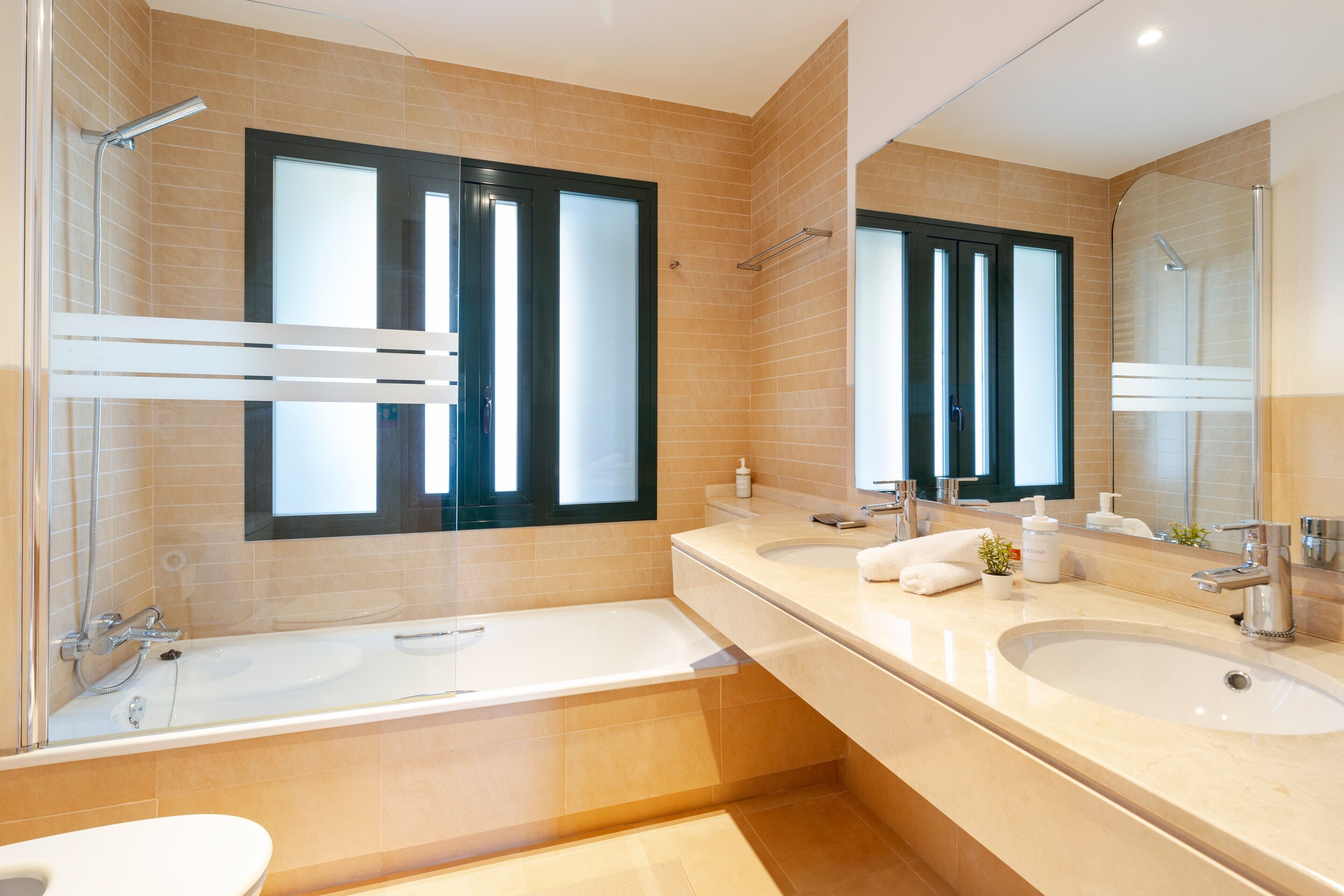 A modern bathroom with a glass shower enclosure, a large bathtub, two sinks, and a mirror above the vanity.