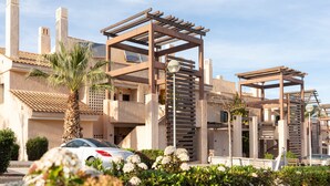 A modern building with a pergola structure, a palm tree, and a car parked in front.