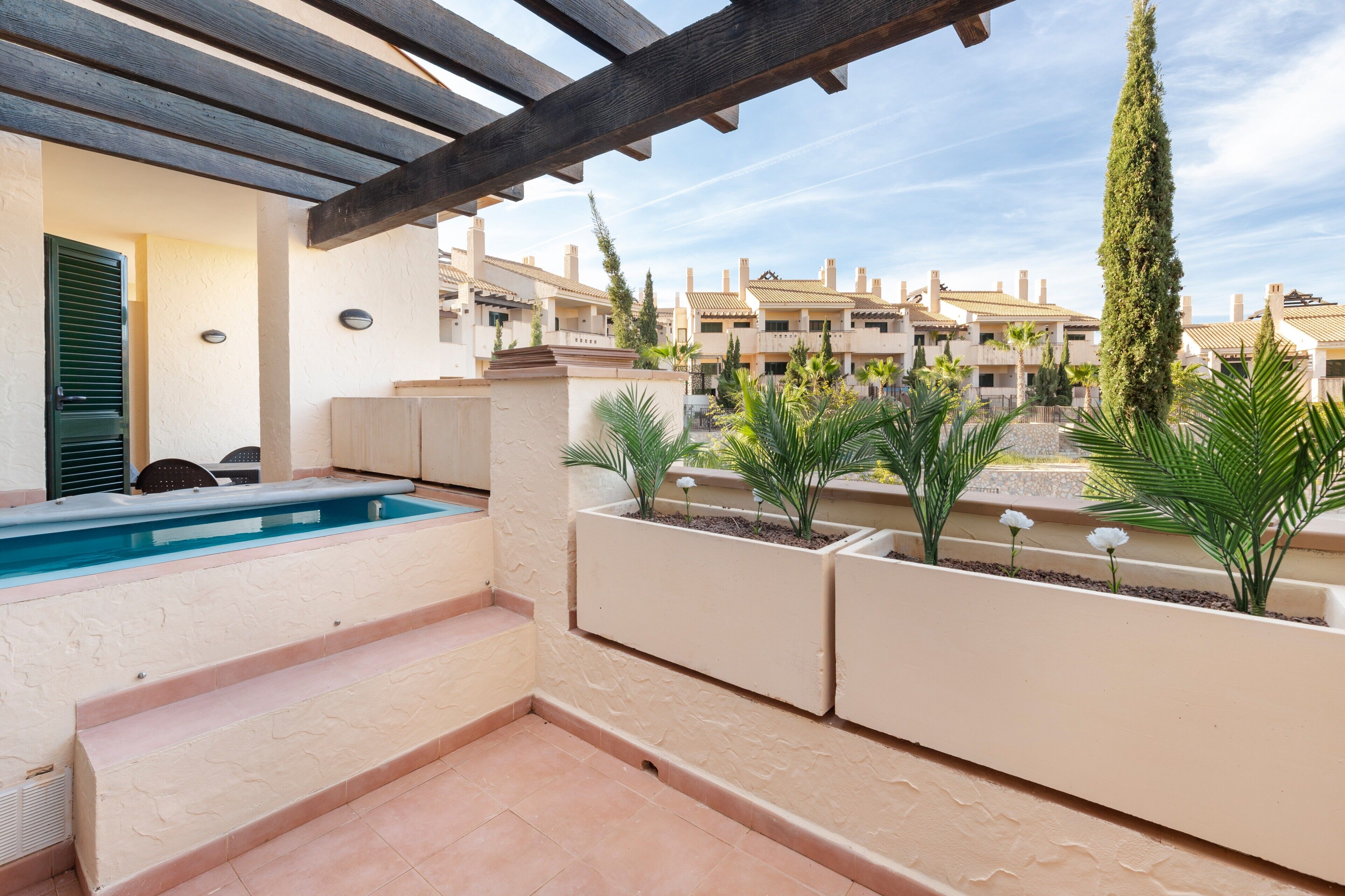 Un espace piscine avec des marches menant à une terrasse, entouré de jardinières et offrant une vue sur des immeubles résidentiels.