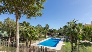 A rectangular swimming pool surrounded by palm trees and a grassy area.