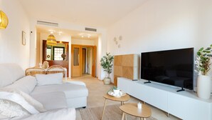 A modern living room with a sectional sofa, a flat-screen TV, a small wooden table, and a large potted plant.