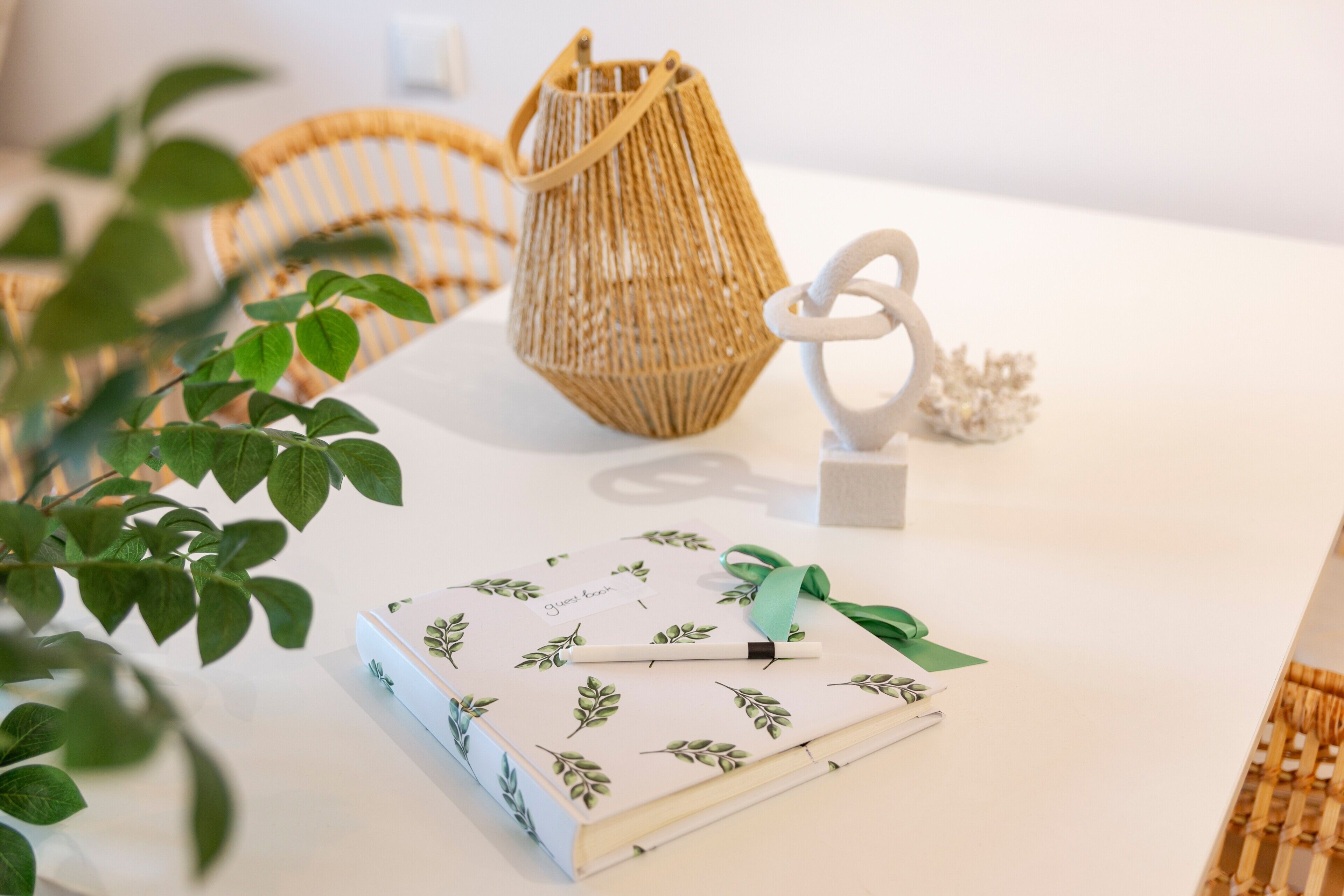 Una mesa blanca con un cuaderno, una cesta de mimbre y una escultura blanca.