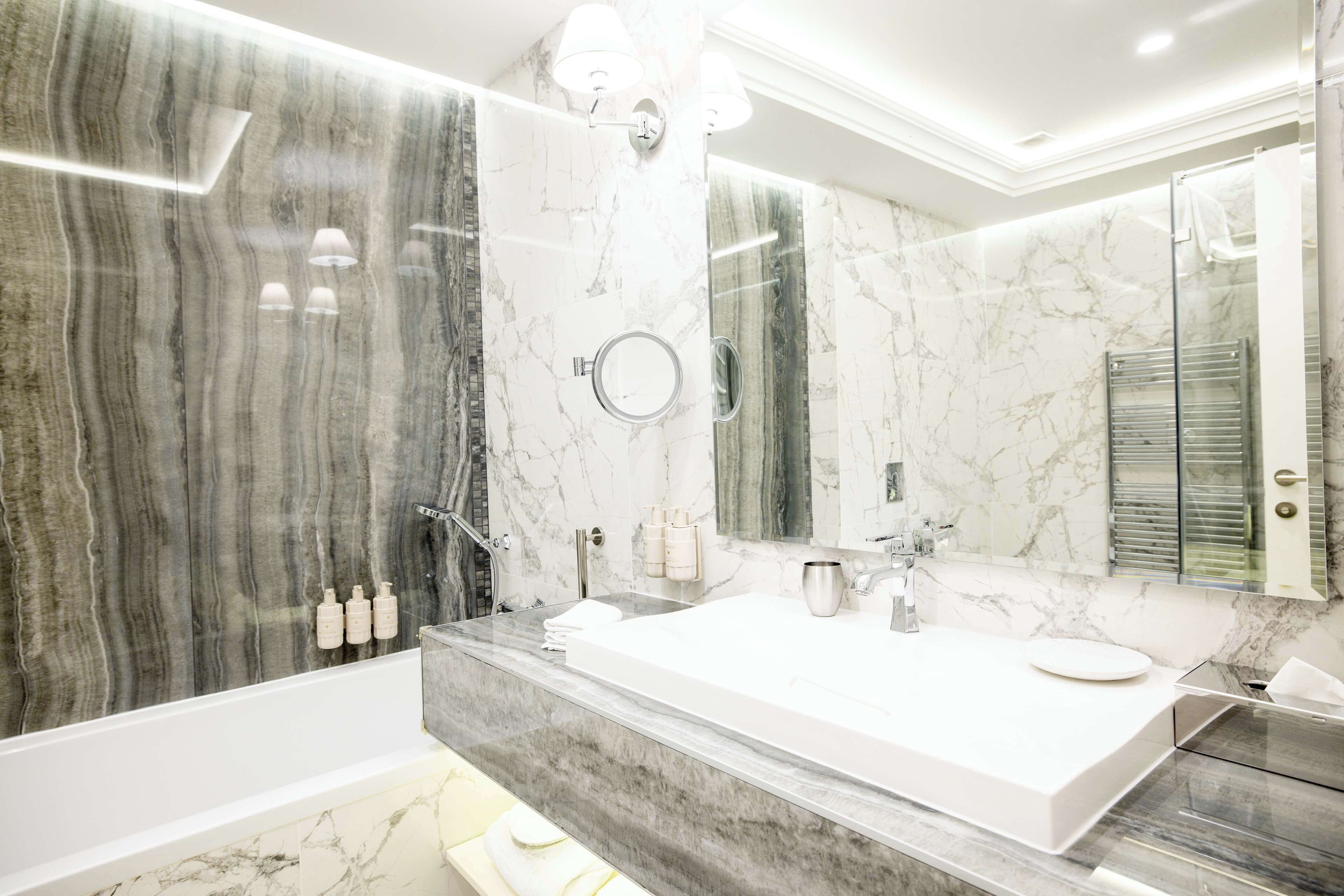 Un baño moderno con un lavabo grande de mármol, una bañera y una ducha con paredes de vidrio.