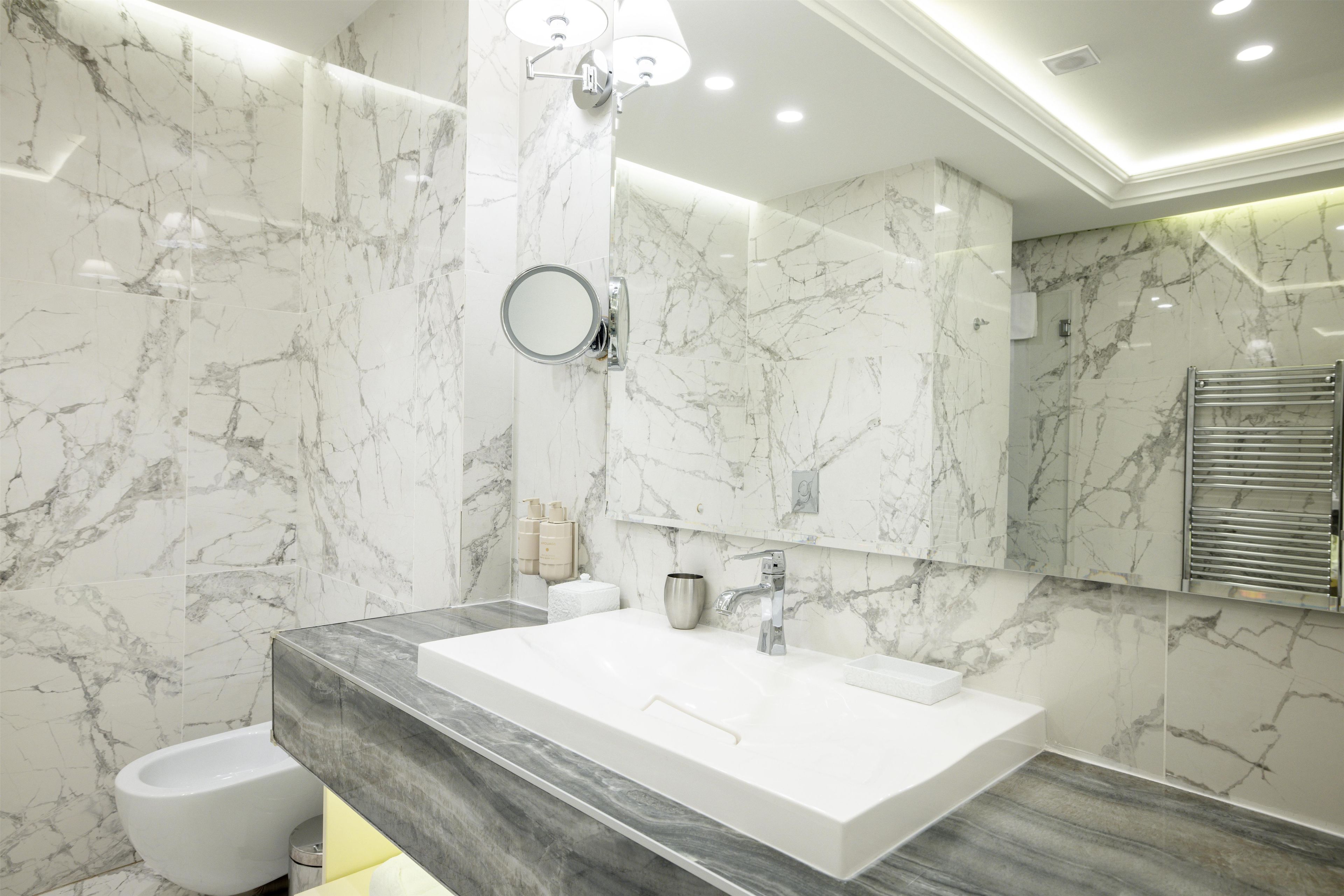 A modern bathroom with a marble vanity, a large mirror, and a separate toilet area.