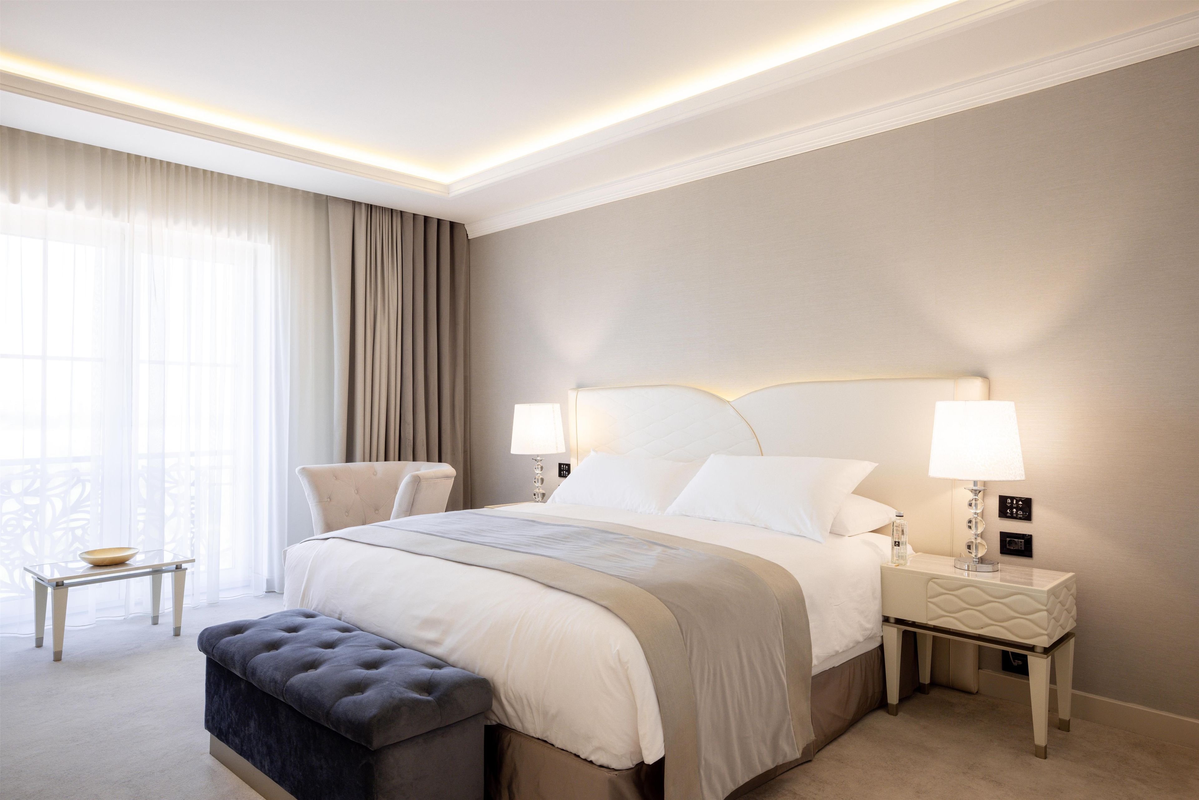 Habitación de hotel con cama, mesitas de noche, un banco y vistas al exterior.