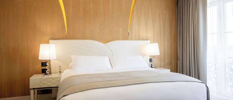 A modern hotel room with a large bed, two bedside lamps, a wooden headboard, and a view of the outdoors.