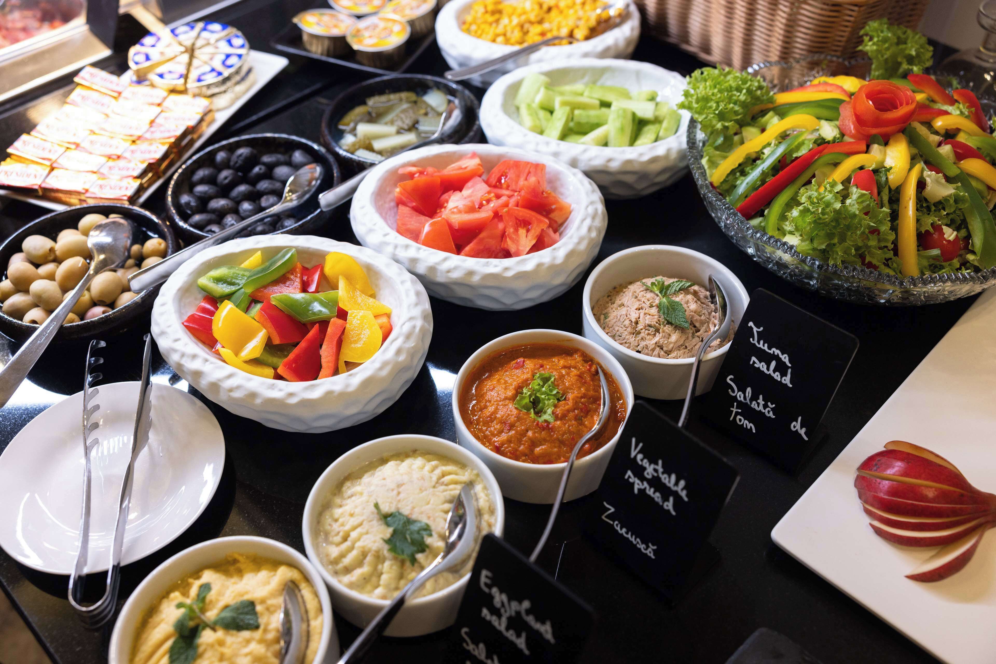 Un bufé con diversos platos, entre ellos ensaladas, salsas y una variedad de verduras.