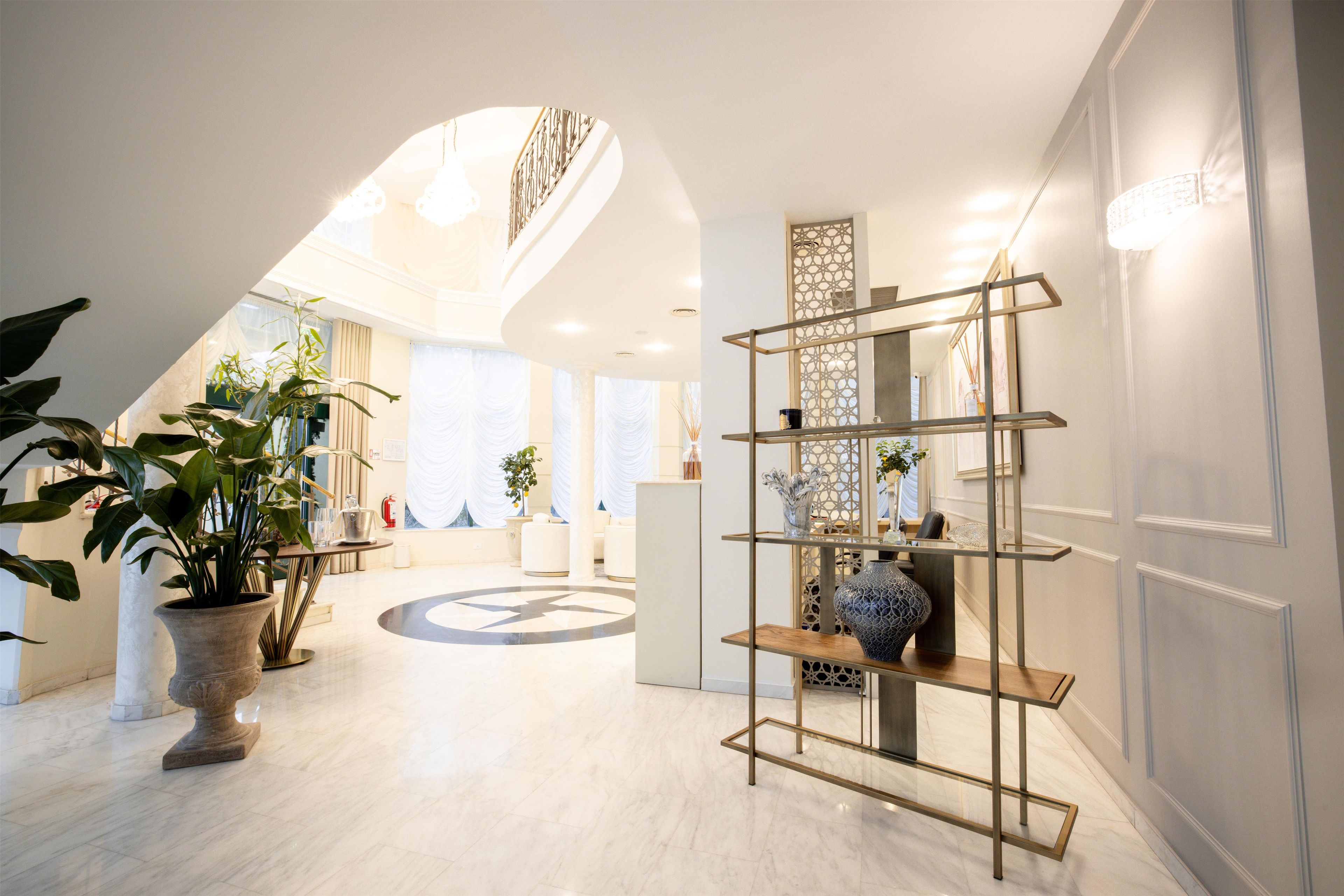 Eine Hotelhalle im modernen Design, mit einem zentralen kreisförmigen Bodenmuster, einer Rezeption und einer dekorativen Metallregaleinrichtung.