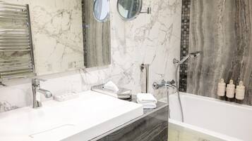 Une salle de bain avec un meuble-lavabo en marbre, deux vasques, un miroir, un porte-serviettes et un espace douche.