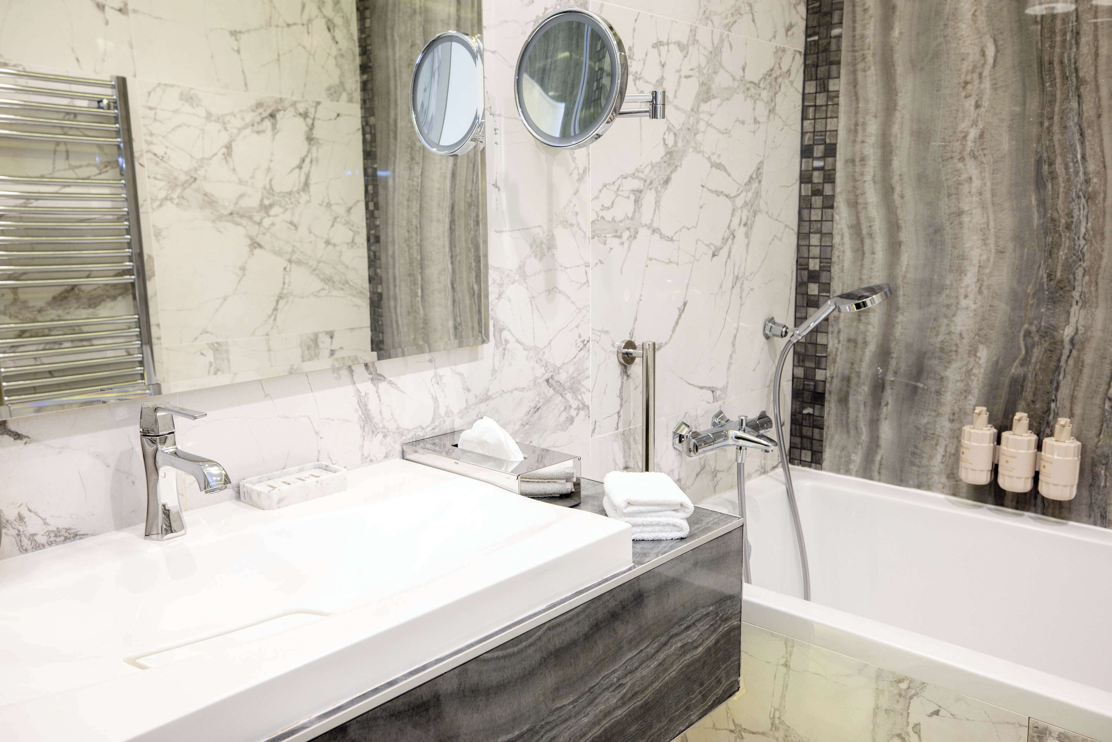 A modern bathroom with two sinks, a large mirror, and a bathtub.