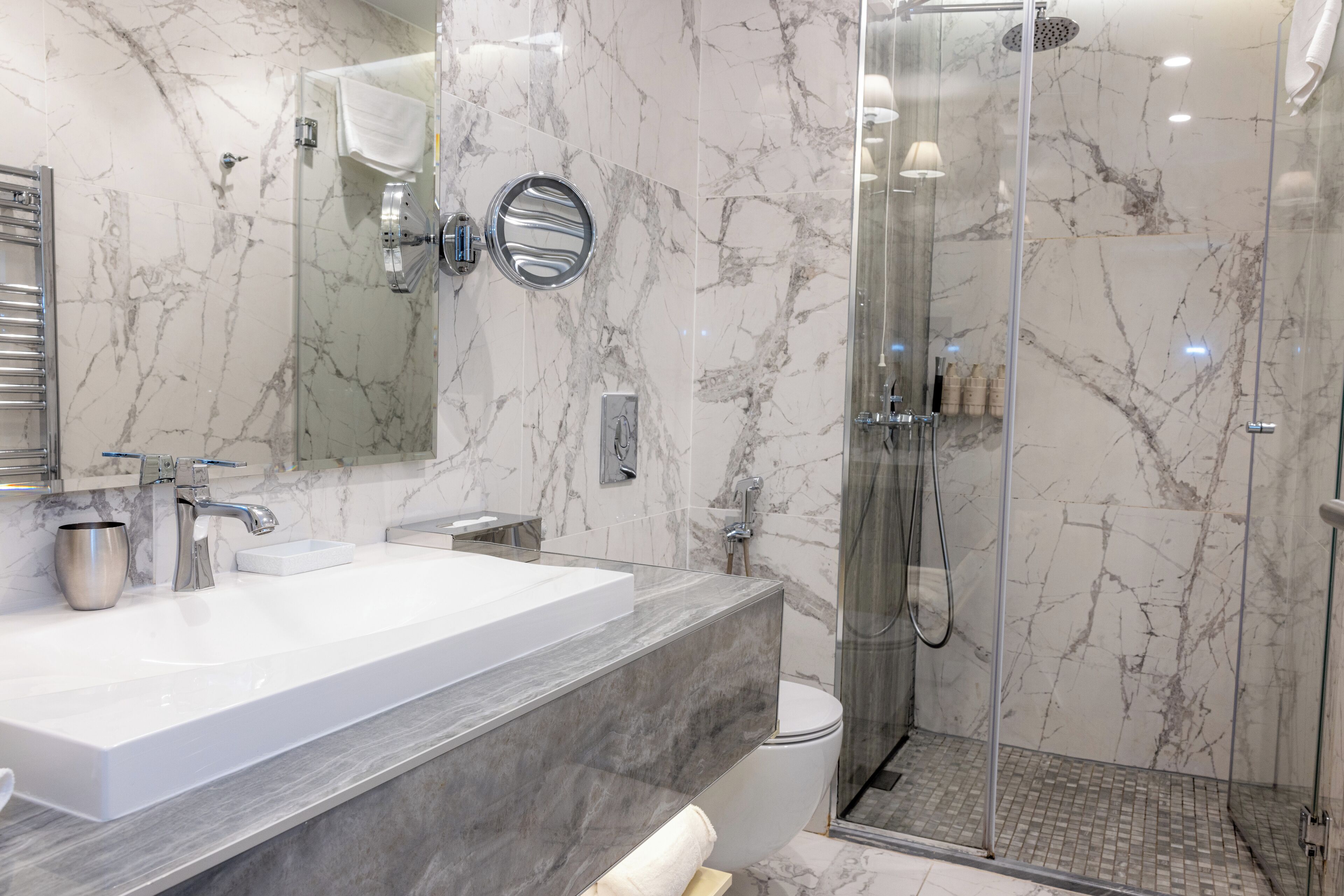 A modern bathroom with a large marble sink, a glass shower enclosure, and a toilet.