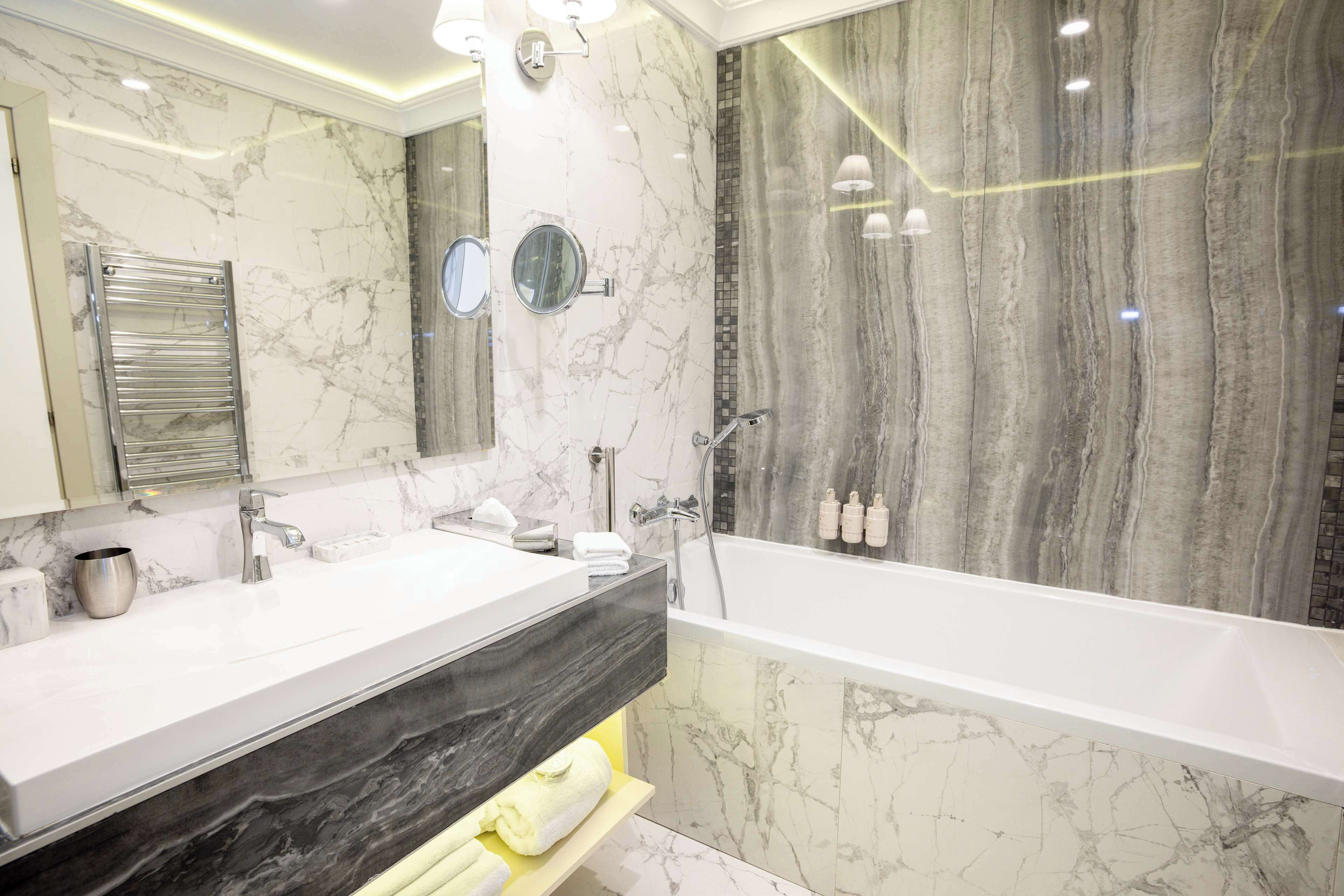 A modern bathroom with a marble vanity, a bathtub, and a large mirror.