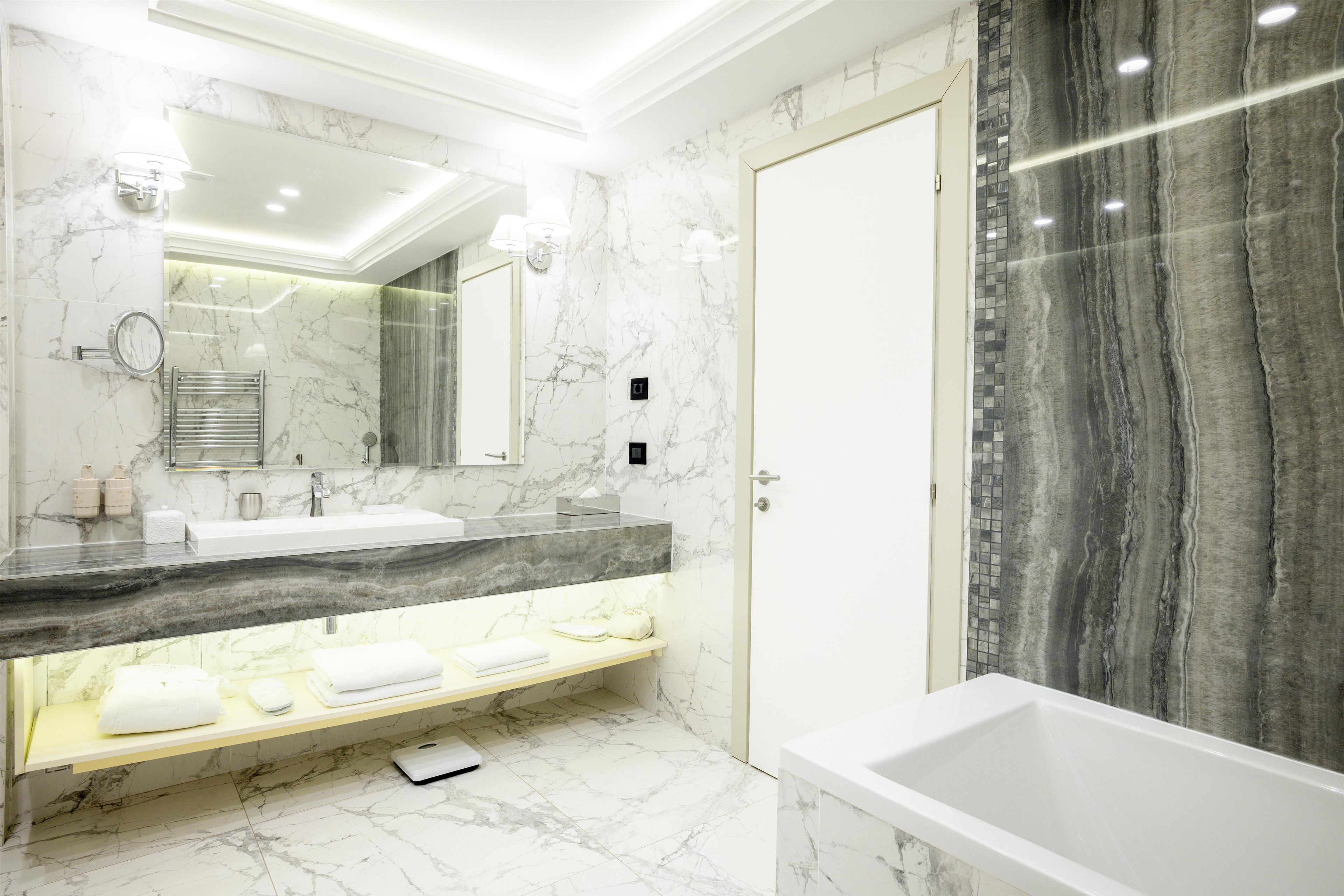 A modern bathroom with a marble vanity, a large mirror, a bathtub, and a towel rack.
