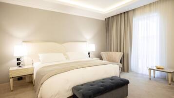 A hotel room with a large bed, bedside lamps, a chair, a small table, and a window with curtains.