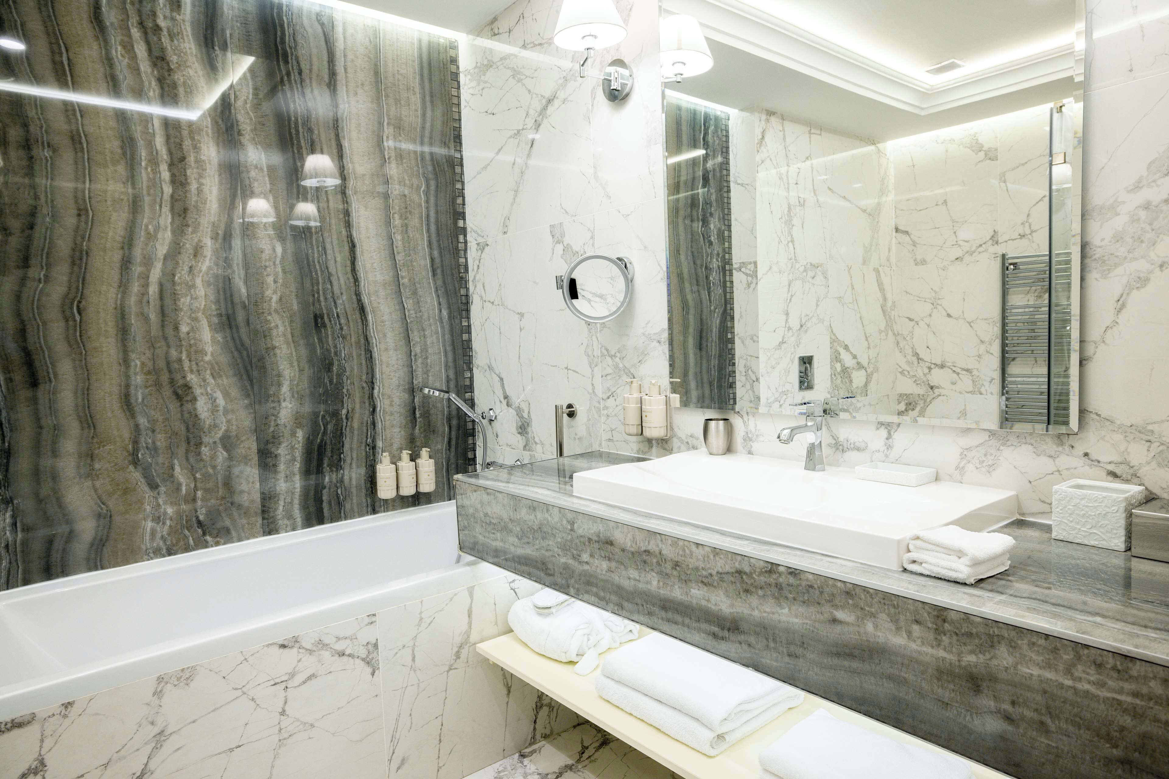 A modern bathroom with a large mirror, two sinks, and a bathtub.