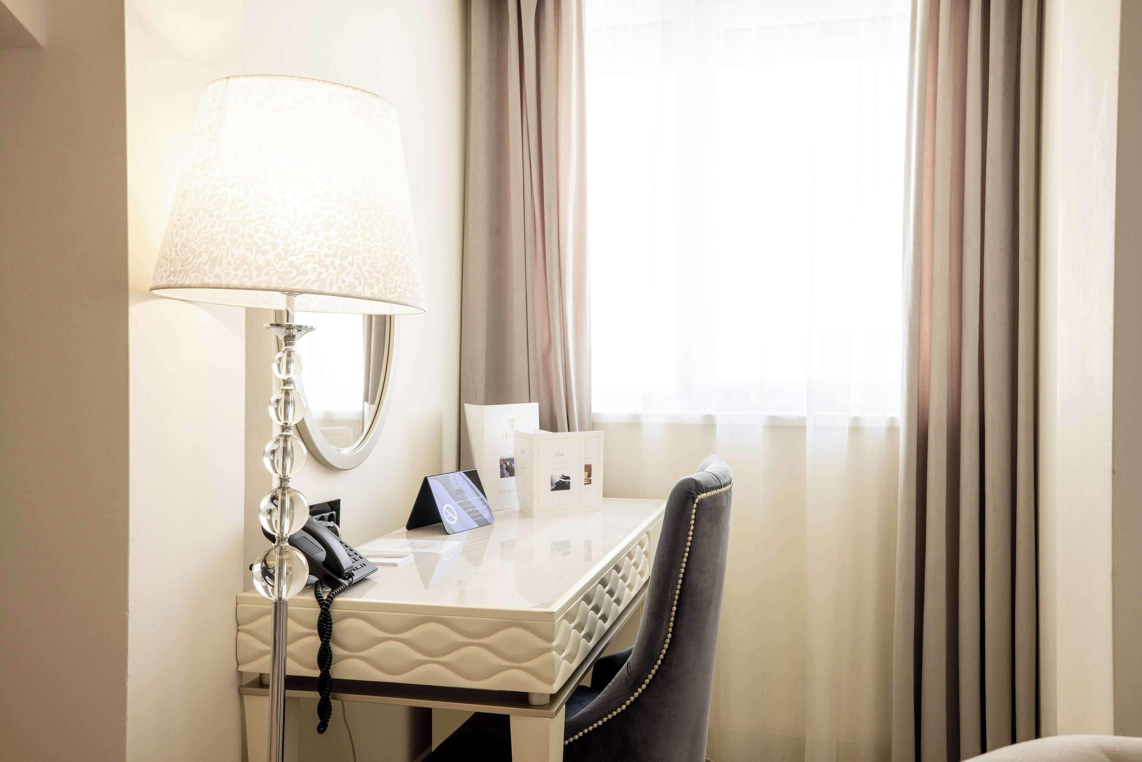 A hotel room with a white desk, a lamp, a telephone, and a chair.