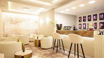 A modern bar area with white sofas, round tables, and a display of liquor bottles.