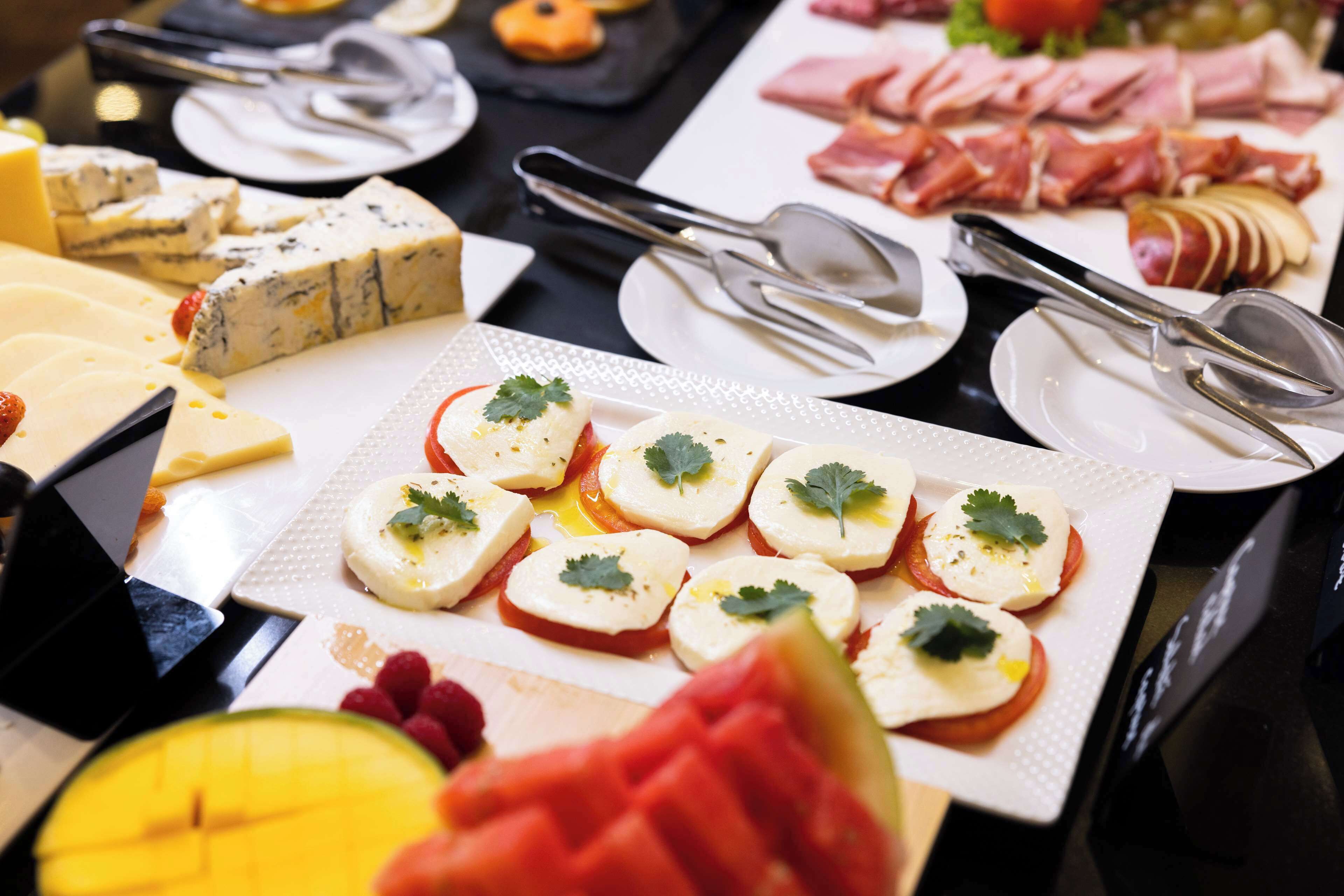 A buffet with various cheeses, meats, and fruit.