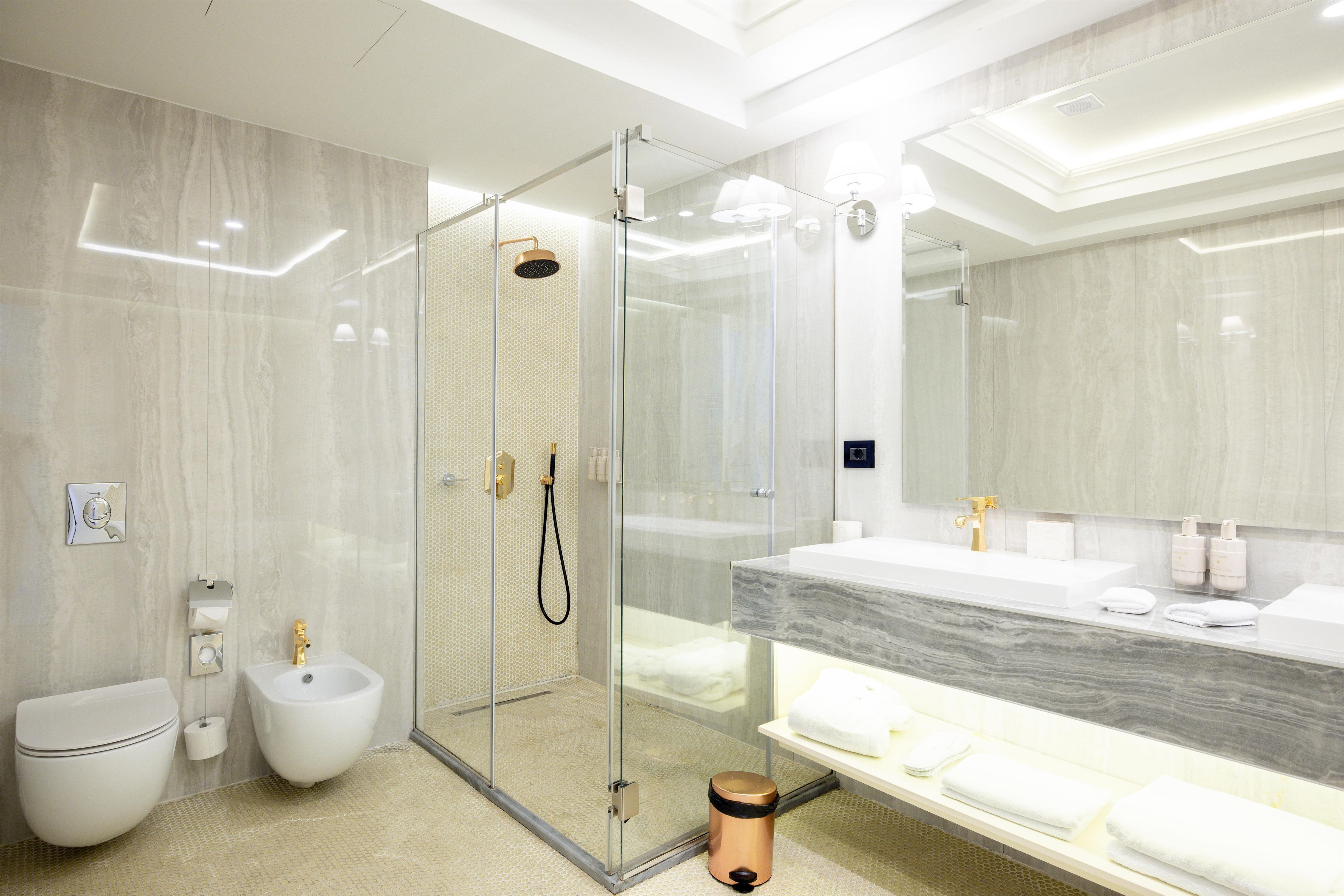 Un baño moderno con ducha envuelta en cristal, tocador de mármol y retrete.