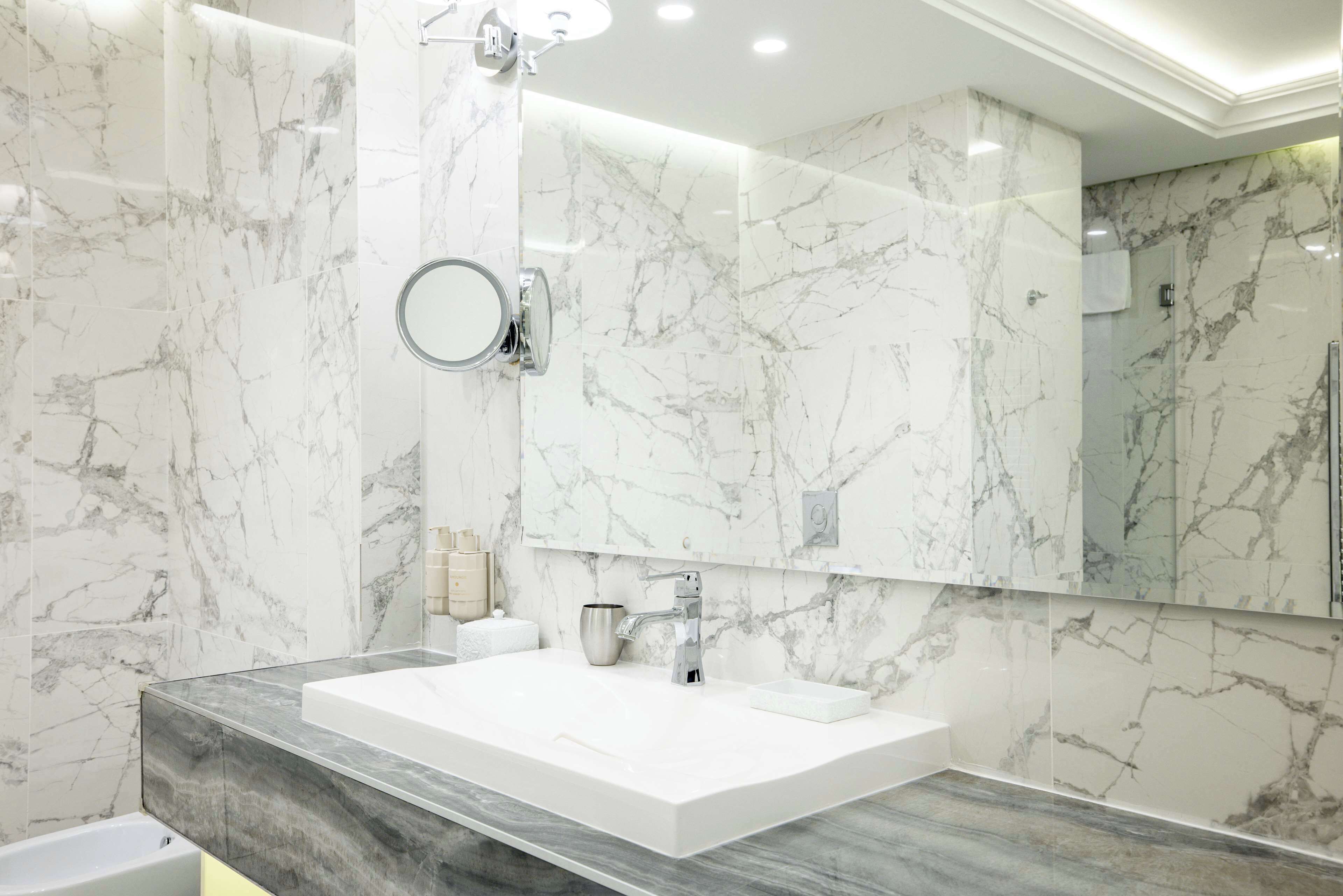 Un baño moderno con una salpicadera de mármol, un espejo grande y un lavamanos blanco.