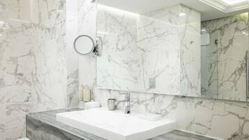 Un baño moderno con una salpicadera de mármol, un espejo grande y un lavamanos blanco.