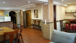 Amplia sala de estar con mesa de comedor, sillas, sofá, zona de cocina con refrigerador y una estantería.